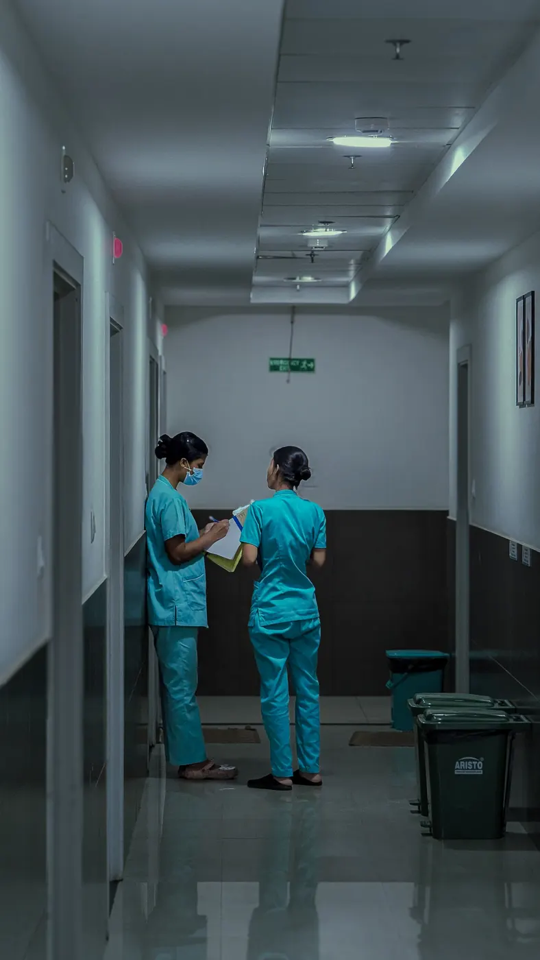 Dua petugas kesihatan berbincang sambil menyemak papan catatan di koridor hospital
