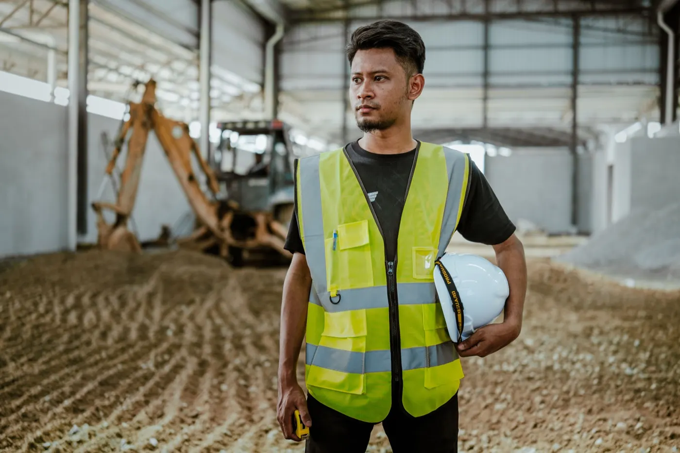Seorang pekerja memakai vest keselamatan sambil memegang topi keselamatan